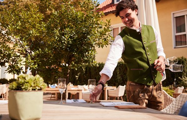: Mann in Tracht deckt Tisch auf Terrasse Brunnenhof Tracht München Restaurant