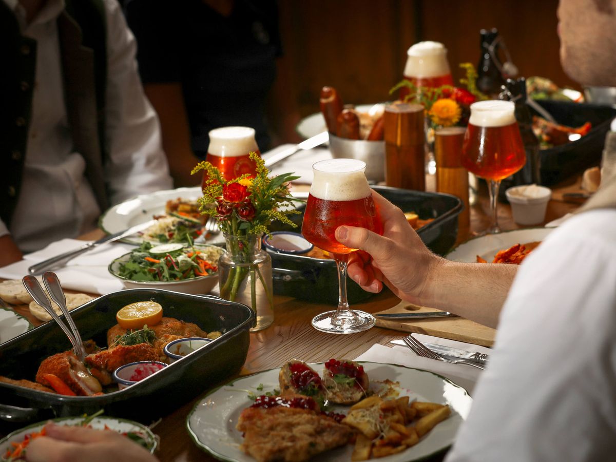: Mann mit Bier in der Hand an einem Tisch mit vielen Gerichten Reich bestückter Tisch im Gasthaus DER BIERMANN